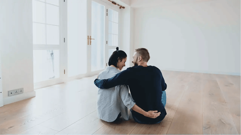 Pareja sentada en el suelo de una vivienda vacía, abrazados mientras estrenan su nuevo hogar, ilustrando qué es el continente en un seguro de hogar.