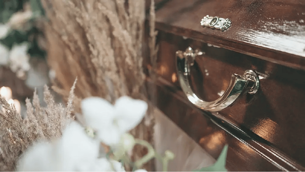 Detalle de un ataúd con flores alrededor, representando el precio de un entierro sin seguro.